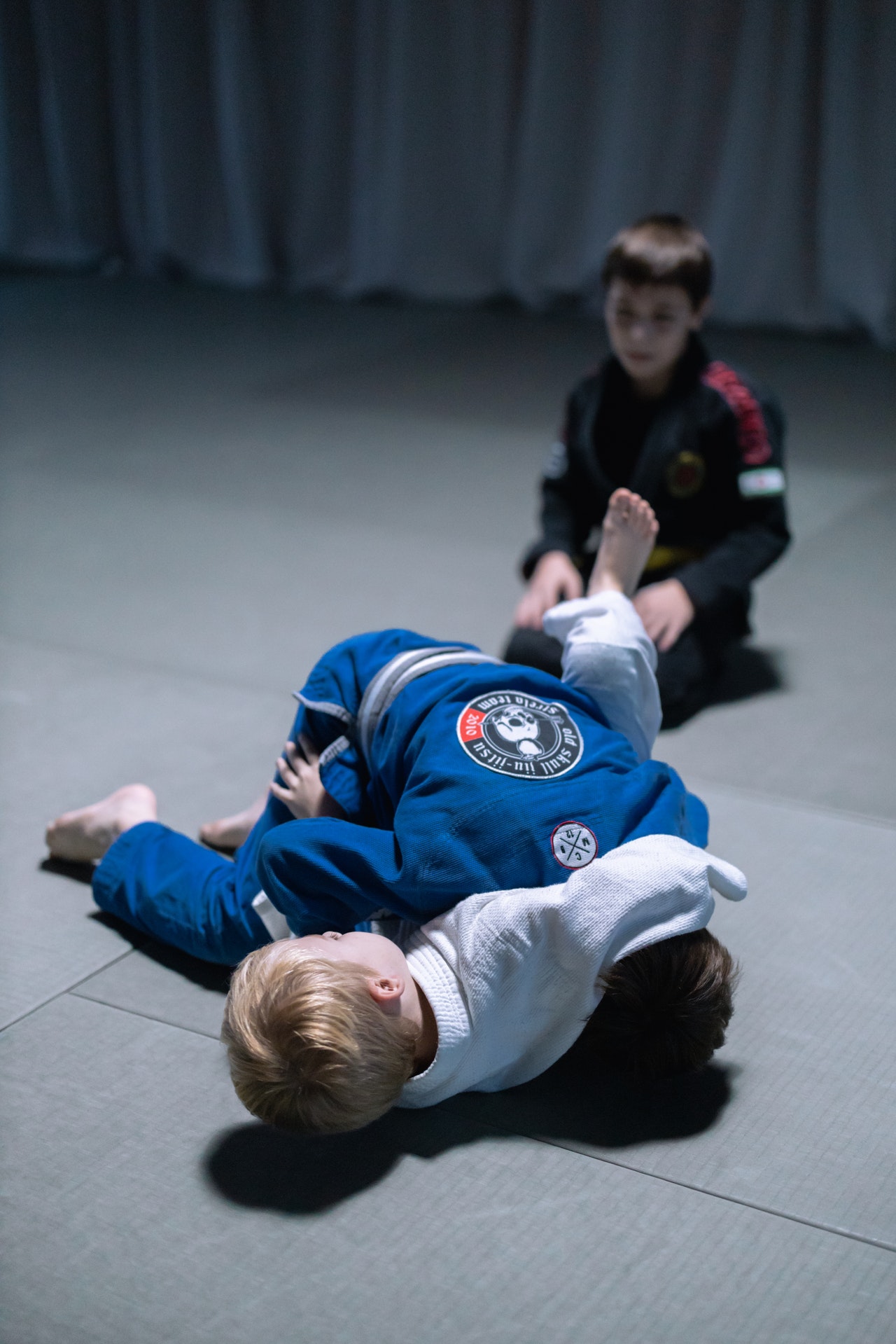 Two children practicing jiu-jitsu and a third child observing the class.